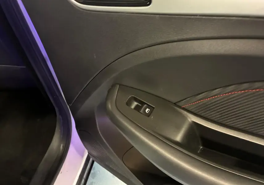 Gros plan sur la porte intérieure côté gauche d’un MG ZS blanc, avec garniture noire et surpiqûres rouges.