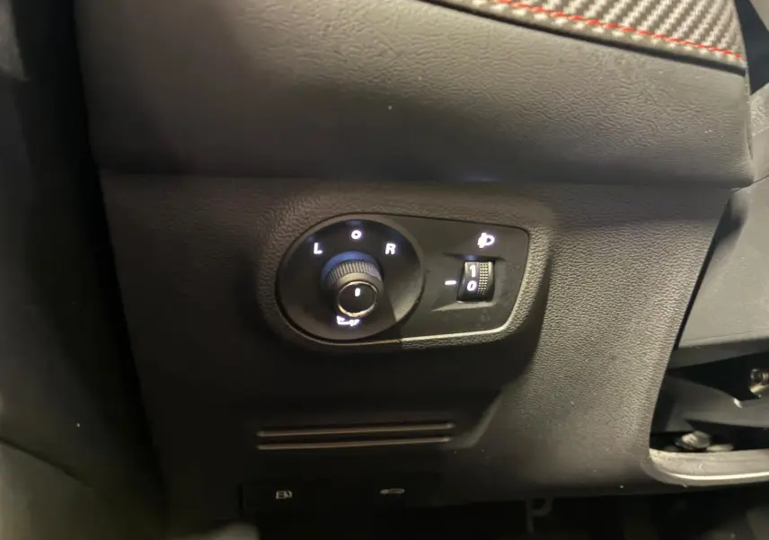 Gros plan sur les commandes de réglage des rétroviseurs et des phares du MG ZS blanc, intérieur noir.