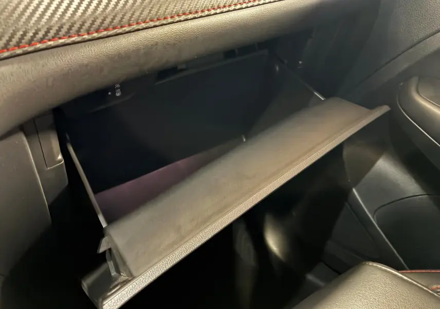 Vue intérieure du vide-poche ouvert côté passager du MG ZS blanc, avec finition cuir noir et surpiqûres rouges.