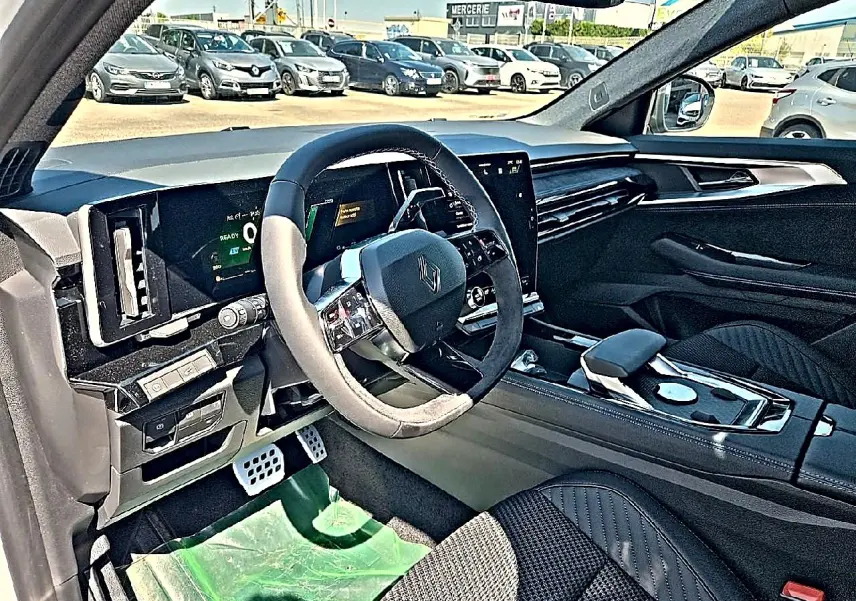 Vue intérieure côté conducteur du Renault Austral blanc nacré, mettant en valeur le volant multifonction et l’écran tactile central.