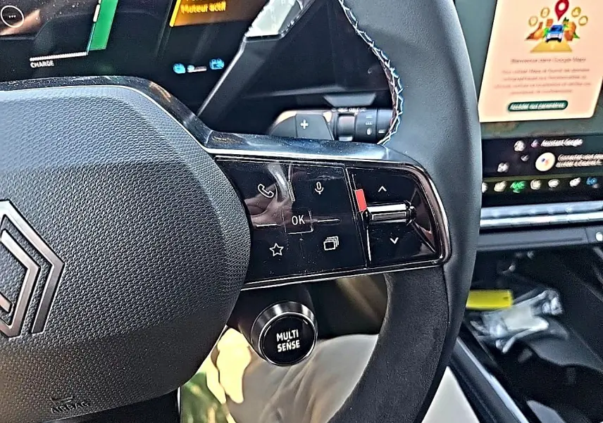 Gros plan sur le volant noir du Renault Austral blanc nacré, avec commandes multifonctions et bouton Multi Sense visible.