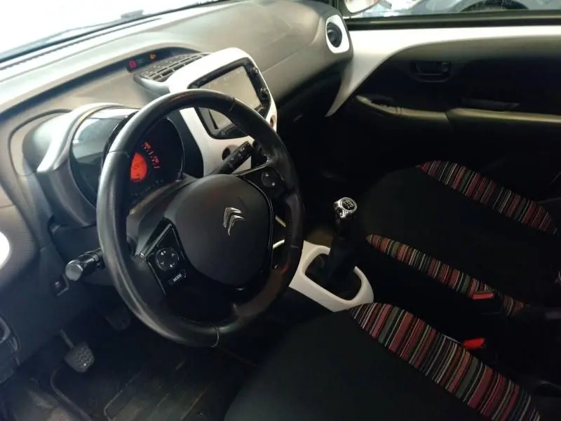 Intérieur de la Citroën C1 blanc, vue côté conducteur montrant volant cuir, tableau de bord et levier de vitesse manuel.