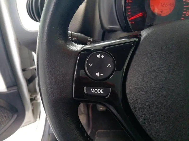 Gros plan sur le volant cuir noir de la Citroën C1 blanc, avec commandes audio intégrées et tableau de bord en arrière-plan.