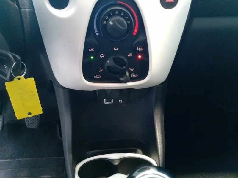 Vue rapprochée du tableau de bord central de la Citroën C1 blanche, avec commandes de climatisation et prise USB visibles.