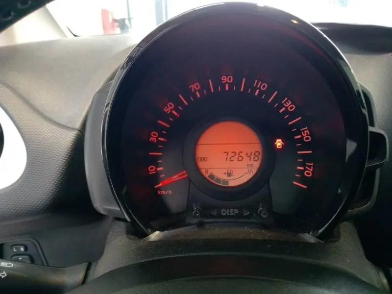 Gros plan sur le compteur de vitesse rougeoyant d'une Citroën C1 blanche, affichant 72 648 km et témoin de porte ouverte.