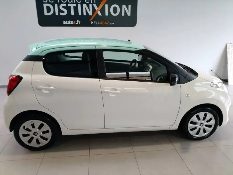 Profil droit d'une Citroën C1 blanche 5 portes avec toit vert clair et enjoliveurs noirs en intérieur showroom.