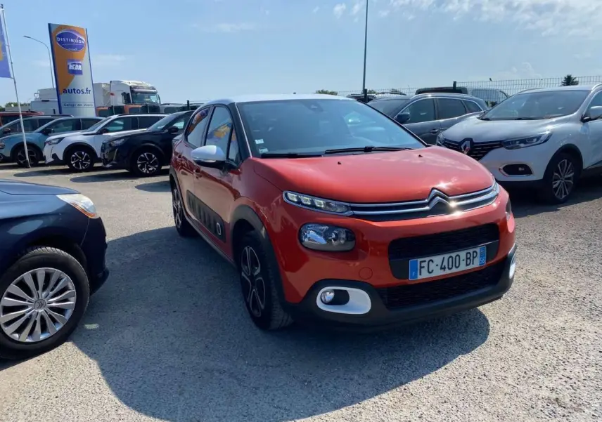 Citroën C3 orange vue 3/4 avant droit avec protections latérales noires et toit noir dans un parking.