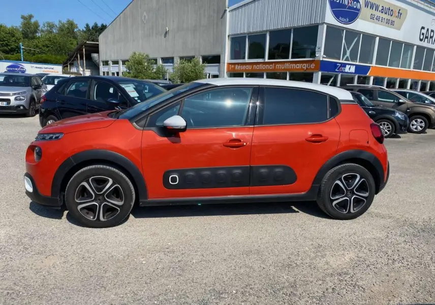 Profil côté gauche d'une Citroën C3 orange avec toit blanc et protections latérales noires en concession.