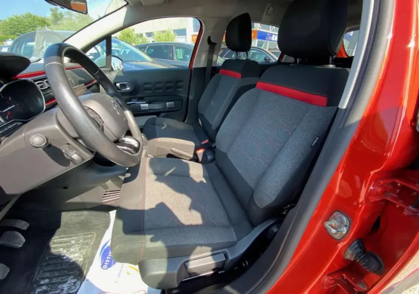 Vue intérieure côté conducteur de la Citroën C3 orange 2018, sièges tissu gris avec surpiqûres rouges et volant noir.