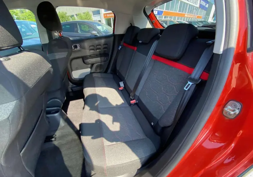 Intérieur arrière de la Citroën C3 orange 2018, banquette tissu gris avec bande rouge et ceintures de sécurité visibles.