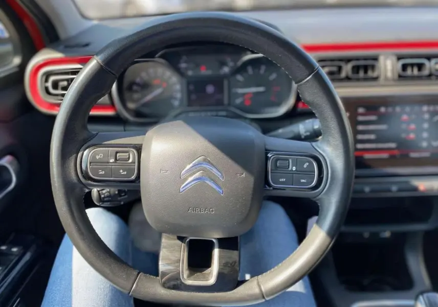 Vue rapprochée du volant noir de la Citroën C3 2018 avec tableau de bord et écran tactile rouge en arrière-plan.