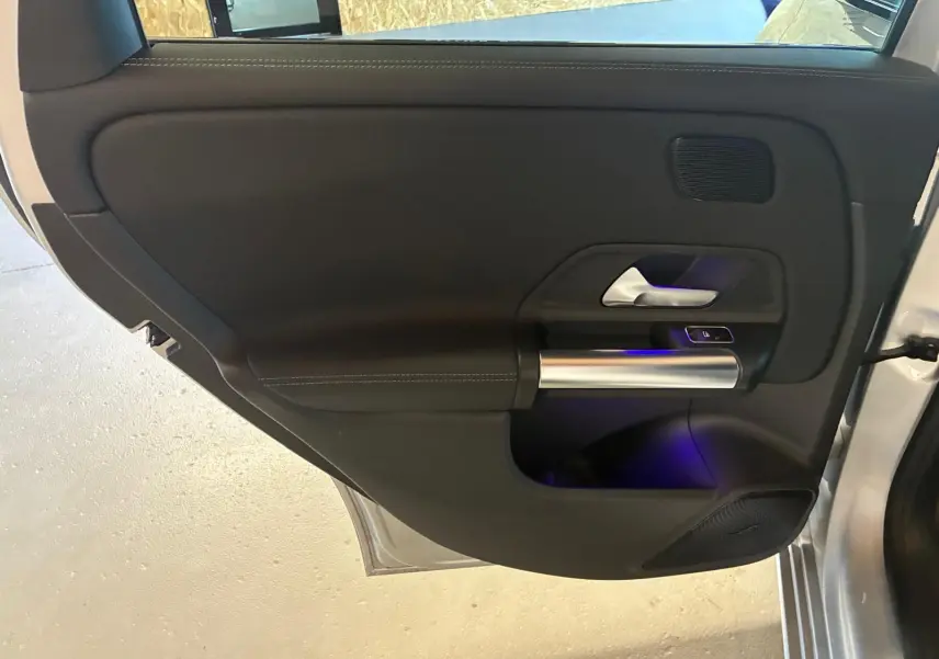 Vue intérieure de la porte arrière droite d'une Mercedes Classe B 200D gris, avec poignée alu et éclairage d'ambiance bleu.