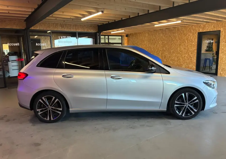 Vue de profil côté gauche d'une Mercedes Classe B 200D Progressive Line gris métallisé, avec jantes alliage et vitres teintées.