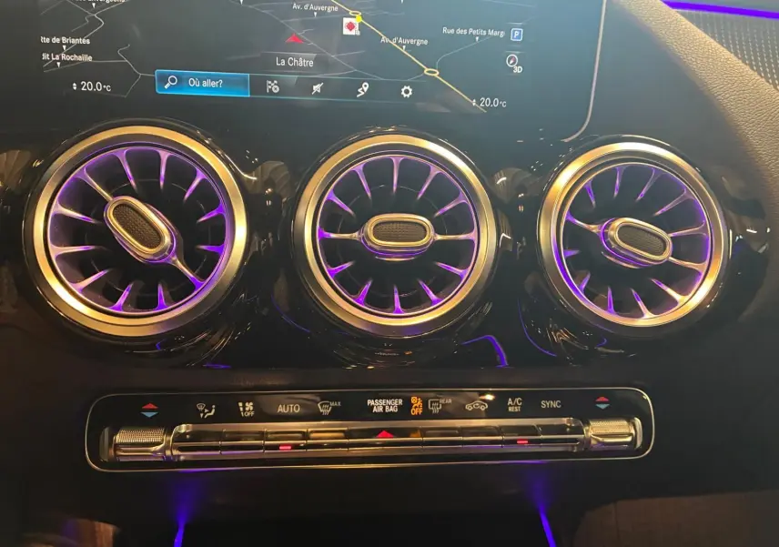 Détail intérieur des aérateurs ronds illuminés en violet et de la console de climatisation d'une Mercedes Classe B 200D 2019 gris.