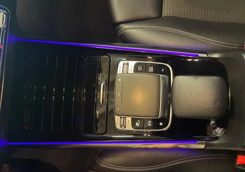 Vue rapprochée du pavé tactile central noir avec éclairage d'ambiance violet dans l'intérieur gris-noir d'une Mercedes Classe B 200D 2019.