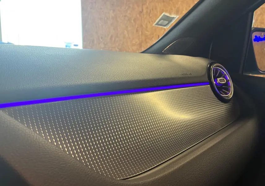 Détail de la planche de bord gris foncé de la Mercedes Classe B 200D avec éclairage d'ambiance bleu et sortie d'air ronde.