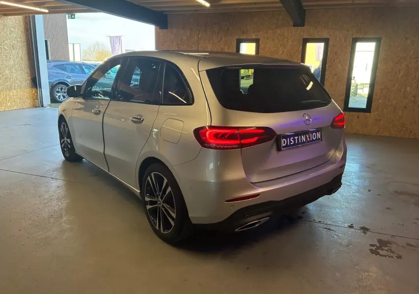 Vue 3/4 arrière droite d'une Mercedes Classe B 200D Progressive Line gris métallisé, feux arrière allumés, en intérieur.