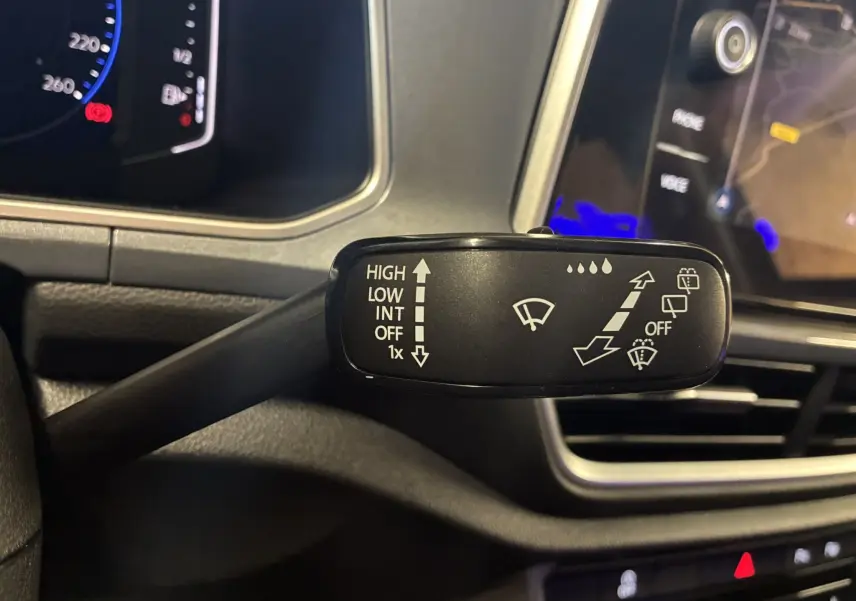 Gros plan sur la commande des essuie-glaces du Volkswagen T-Roc noir, tableau de bord et écran tactile en arrière-plan.