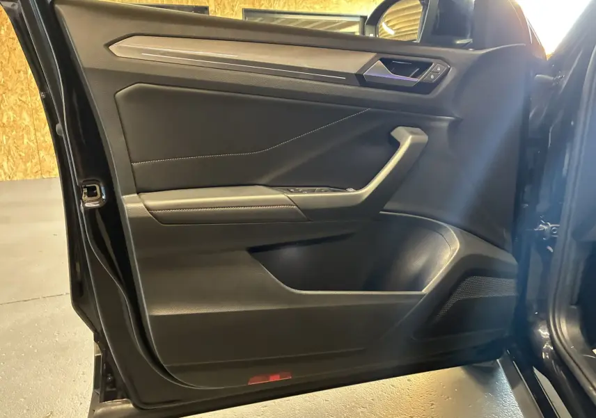 Vue intérieure de la porte avant gauche noire du Volkswagen T-Roc 2025 avec garniture tissu et détails en plastique.