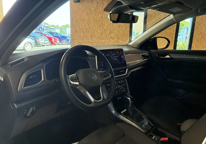 Vue intérieure côté conducteur du Volkswagen T-Roc noir 2025, mettant en valeur le volant multifonction et l'écran tactile central.