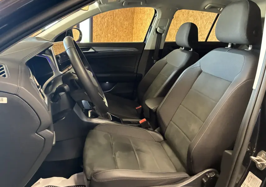 Vue intérieure côté gauche du Volkswagen T-Roc 2025 noir, montrant les sièges avant en tissu noir et le tableau de bord moderne.