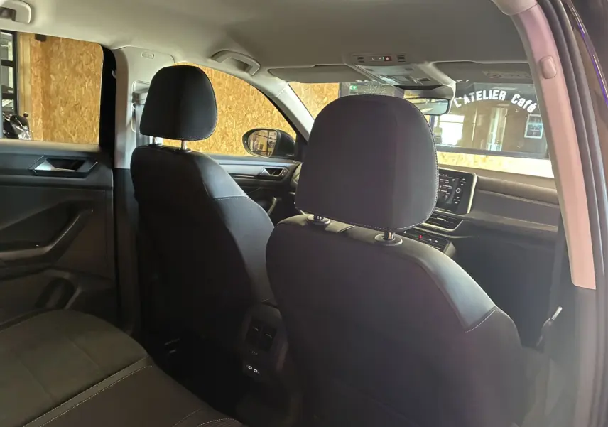Vue intérieure arrière du Volkswagen T-Roc noir 2025, montrant les sièges avant en tissu noir et la console centrale avec écran tactile.