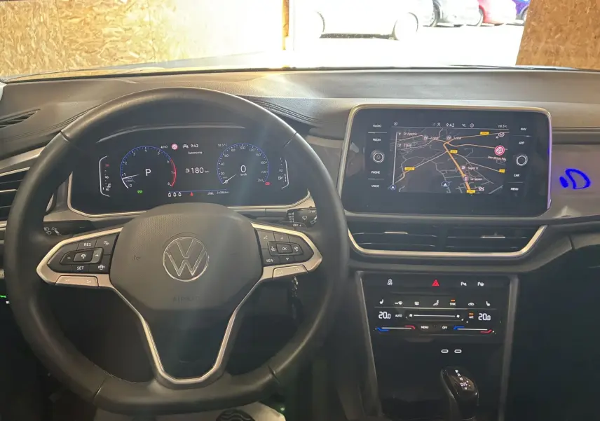 Vue intérieure du tableau de bord noir du Volkswagen T-Roc 2025, avec volant multifonction et écran tactile GPS allumé.