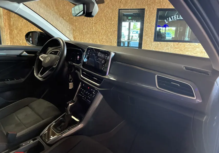 Vue intérieure côté conducteur du Volkswagen T-Roc 2025 noir, mettant en valeur le tableau de bord moderne et l’écran tactile central.
