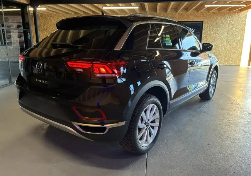 Vue 3/4 arrière droite du Volkswagen T-Roc noir 2025, avec feux arrière allumés et jantes alliage visibles.