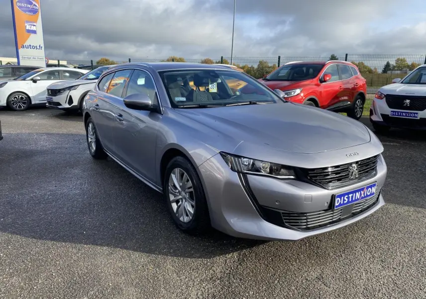 Peugeot 508 SW gris Artense vue 3/4 avant droit sur parking avec calandre noire et jantes alu.