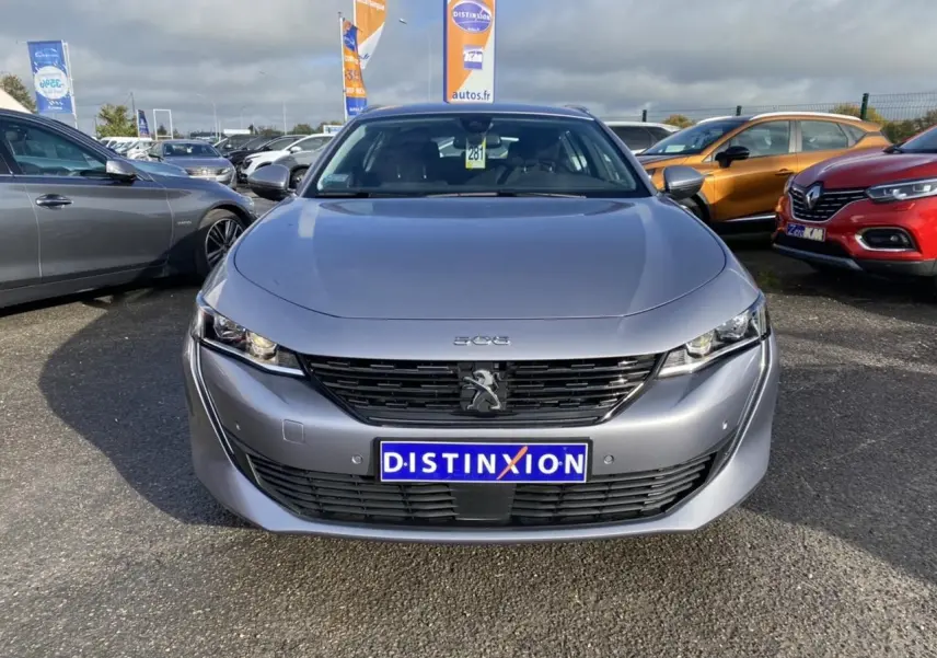 Vue frontale d'une Peugeot 508 SW gris Artense avec calandre noire et logo lion au centre, stationnée en extérieur.