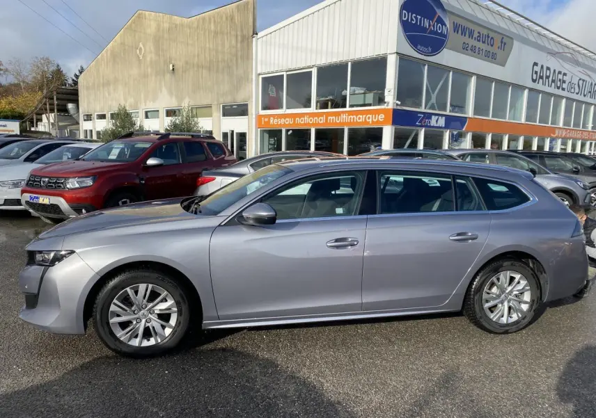 Profil droit d'une Peugeot 508 SW gris Artense 2021 stationnée devant un garage multimarque.