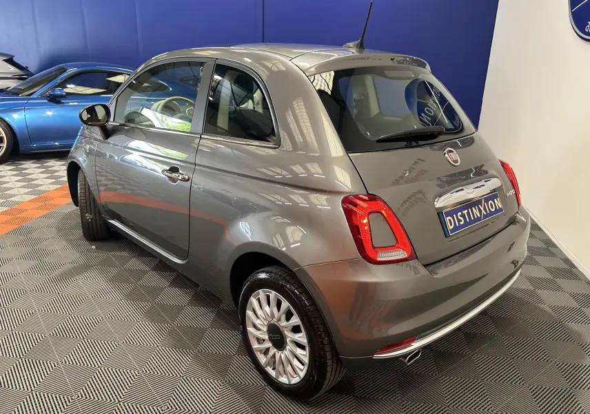 Vue 3/4 arrière droite d'une FIAT 500 gris métallisé avec toit panoramique, en intérieur showroom.