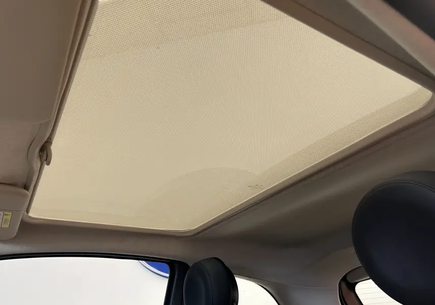 Vue intérieure du toit panoramique avec pare-soleil déployé et appuie-tête en cuir noir d'une Fiat 500 grise.