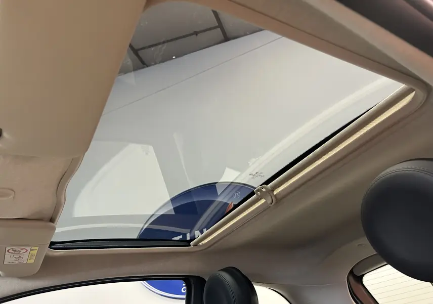 Toit panoramique ouvert vu de l'intérieur côté gauche d'une Fiat 500 gris clair avec sièges en cuir noir.