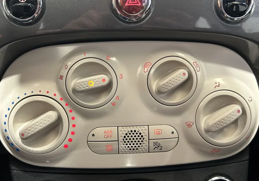 Gros plan sur les commandes de climatisation et ventilation de la Fiat 500 gris, montrant les boutons rotatifs et indicateurs rouges et bleus.