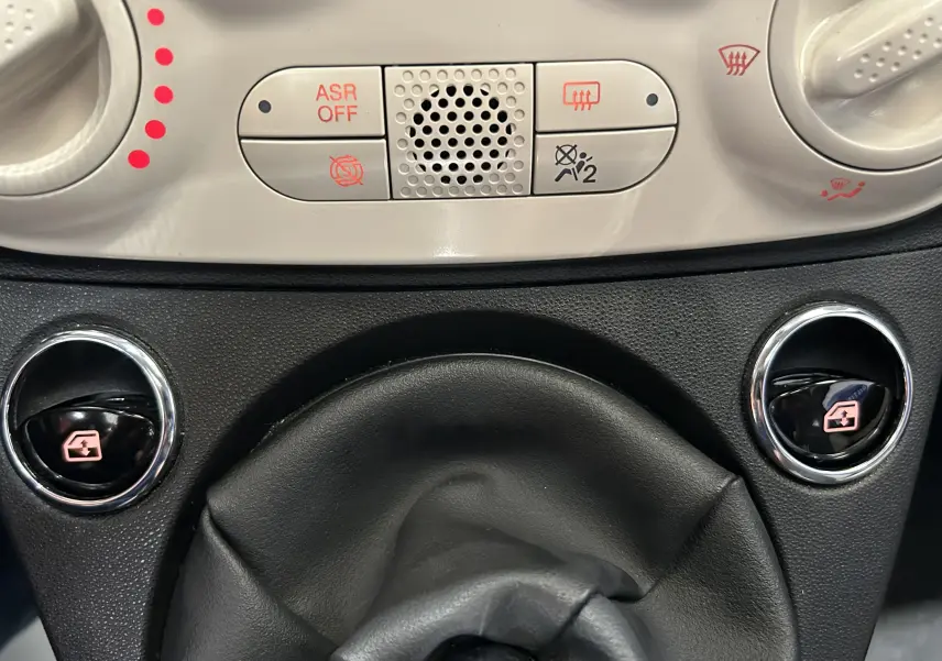 Gros plan sur la console centrale de la Fiat 500 gris 2022, montrant les commandes de climatisation et les boutons de lève-vitres.