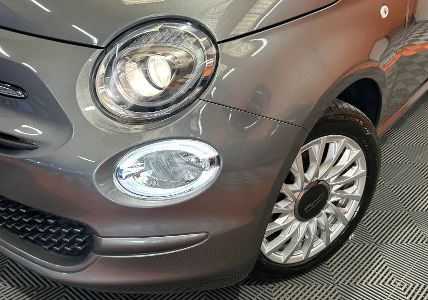 Gros plan sur l'avant droit gris métallisé d'une FIAT 500 avec phare rond et jante alliage élégante.