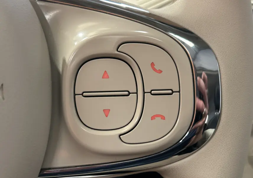 Gros plan sur les commandes de téléphone et volume sur le volant beige d'une Fiat 500 70 Hybride BSG Dolcevita 2022.