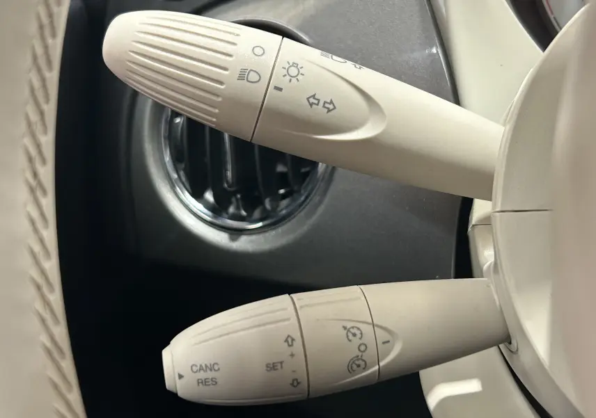 Gros plan sur les commandes de clignotants et régulateur de vitesse beiges du tableau de bord d'une FIAT 500 gris 2022.