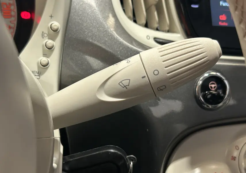 Gros plan sur la manette d’essuie-glace beige à gauche du volant dans l’habitacle gris clair d’une Fiat 500 70 Hybride BSG DolceVita.