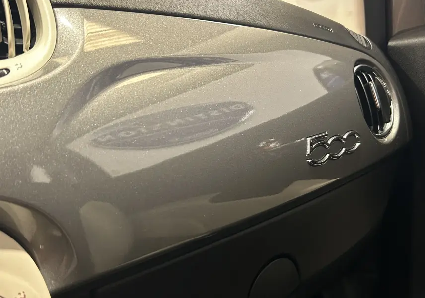 Détail du tableau de bord gris métallisé de la Fiat 500 avec logo 500 et sortie d'air ronde à droite.