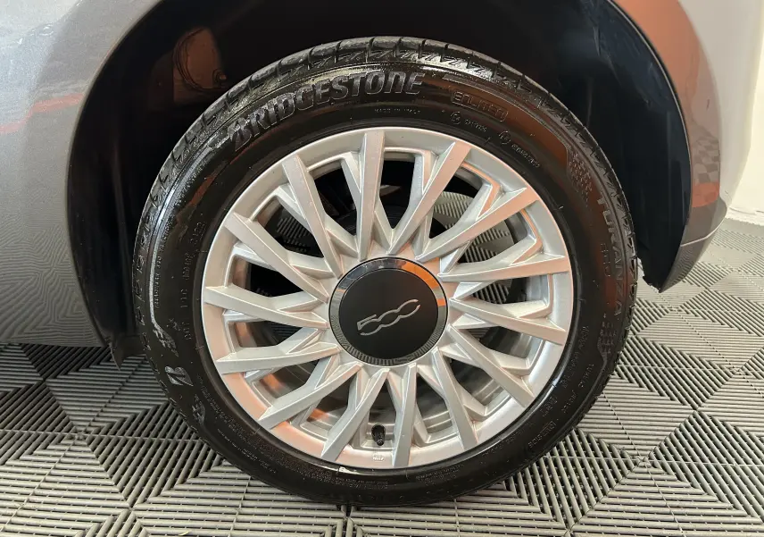 Gros plan sur la roue avant droite gris métallisé de la FIAT 500 70 Hybride BSG DolceVita avec jante argentée et logo 500.