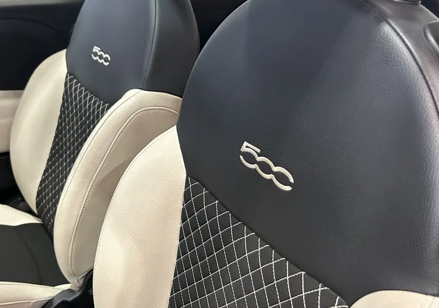Gros plan sur les sièges avant bicolores noir et beige avec logo 500 brodé, intérieur du Fiat 500 hybride 2022.