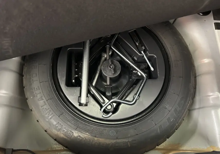Gros plan sur la roue de secours et les outils de bord dans le coffre d'une FIAT 500 gris 70 Hybride BSG DolceVita 2022.