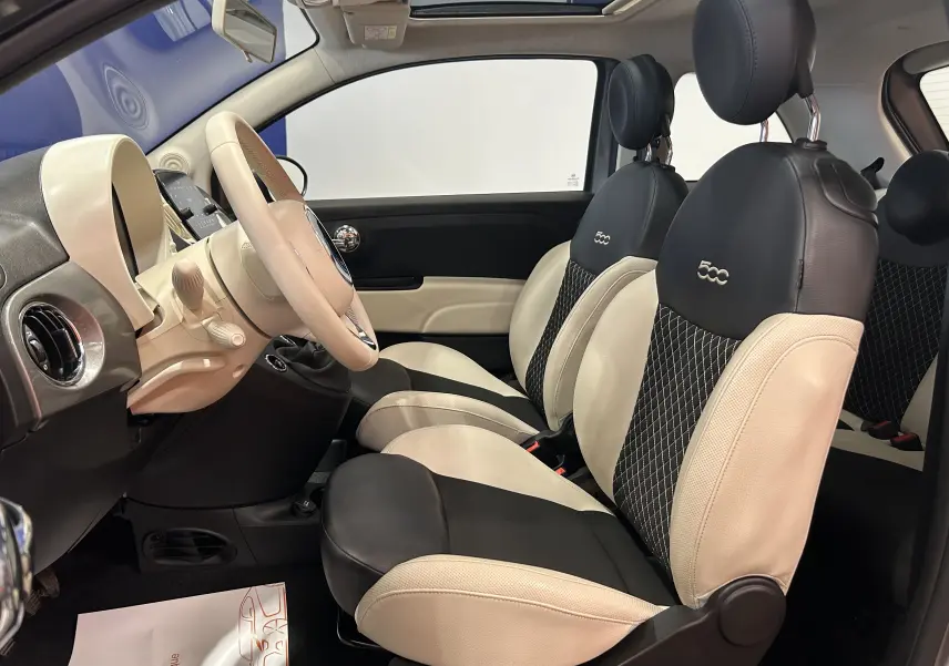 Vue intérieure côté gauche de la Fiat 500 hybride 2022 avec sièges cuir bicolores noir et blanc et toit panoramique.