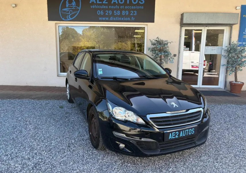 Peugeot 308 Active noire vue en 3/4 avant droit, stationnée devant un garage AE2 Autos sur gravier.