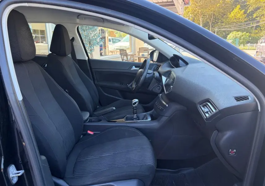 Vue intérieure côté conducteur de la Peugeot 308 noire de 2014, montrant les sièges et la boîte manuelle.