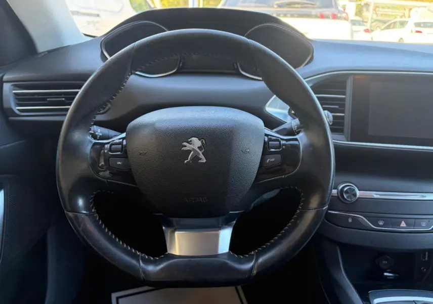 Vue rapprochée du volant noir de la Peugeot 308 Active 2014 avec tableau de bord et écran tactile en arrière-plan.