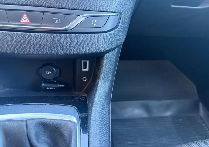 Gros plan sur la console centrale intérieure noire d'une Peugeot 308 Active 2014, avec prise 12V, port USB et commande de climatisation.